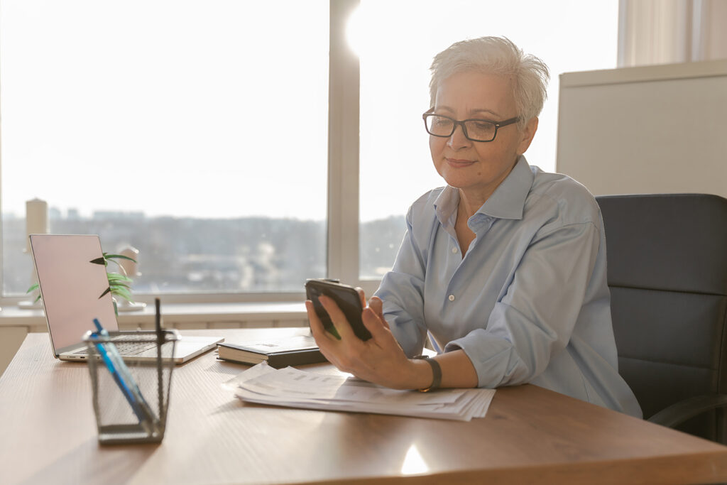 Business professional reviewing messages on a smartphone at her desk, representing American SurgiSite’s reliable communication and support for surgery centers.