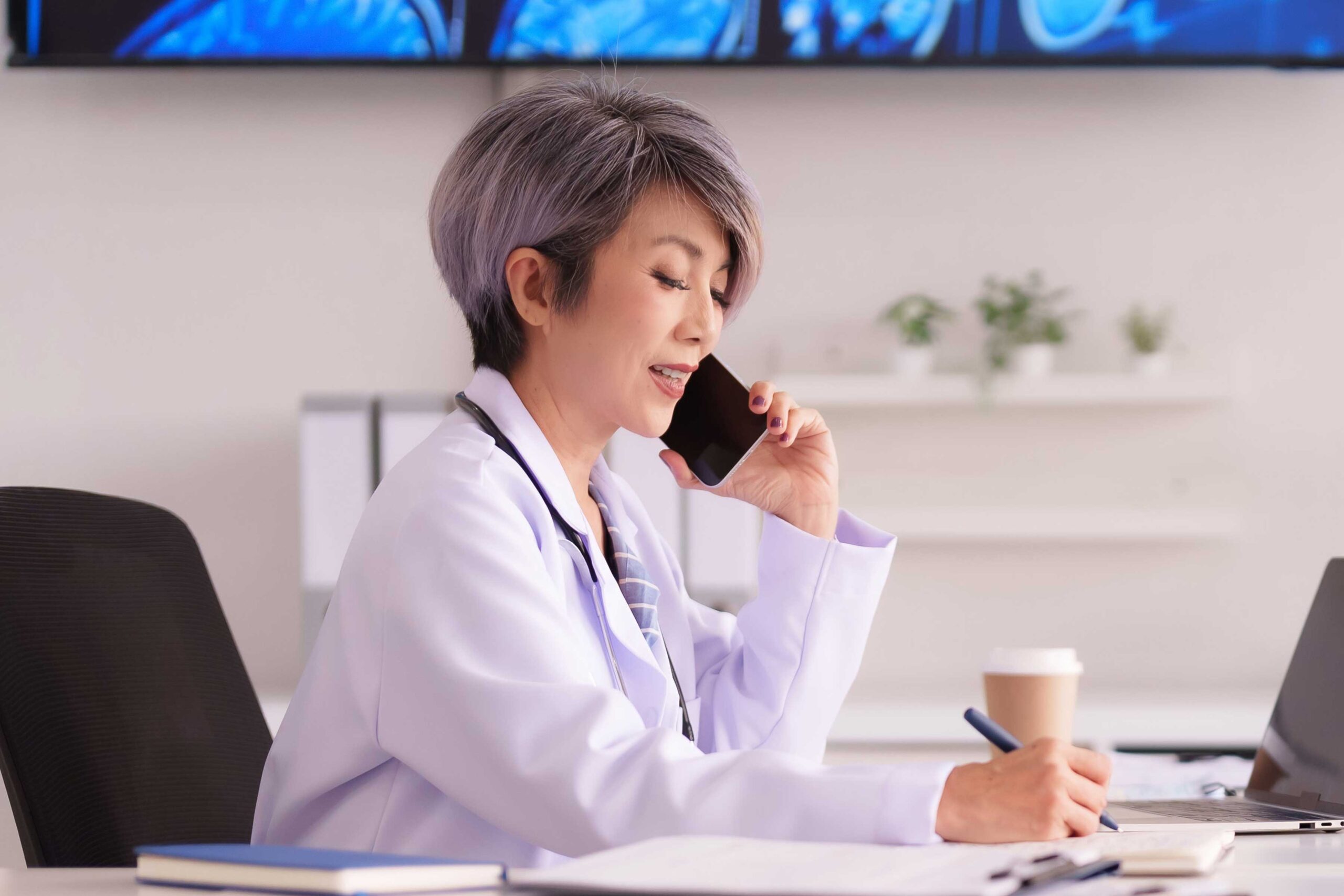Doctor on the phone while working at her desk, representing American SurgiSite’s focus on communication and coordination for surgery center success.